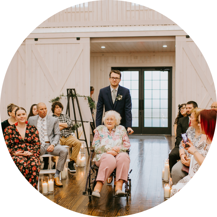 Person using a manual wheelchair is assisted down the aisle of a wedding ceremony